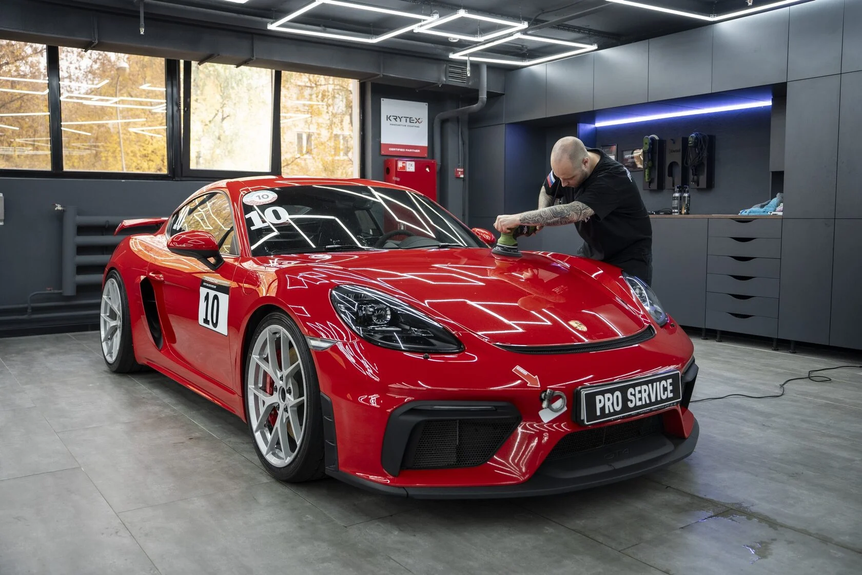 Мастер полирует капот красного Porsche Cayman GT4