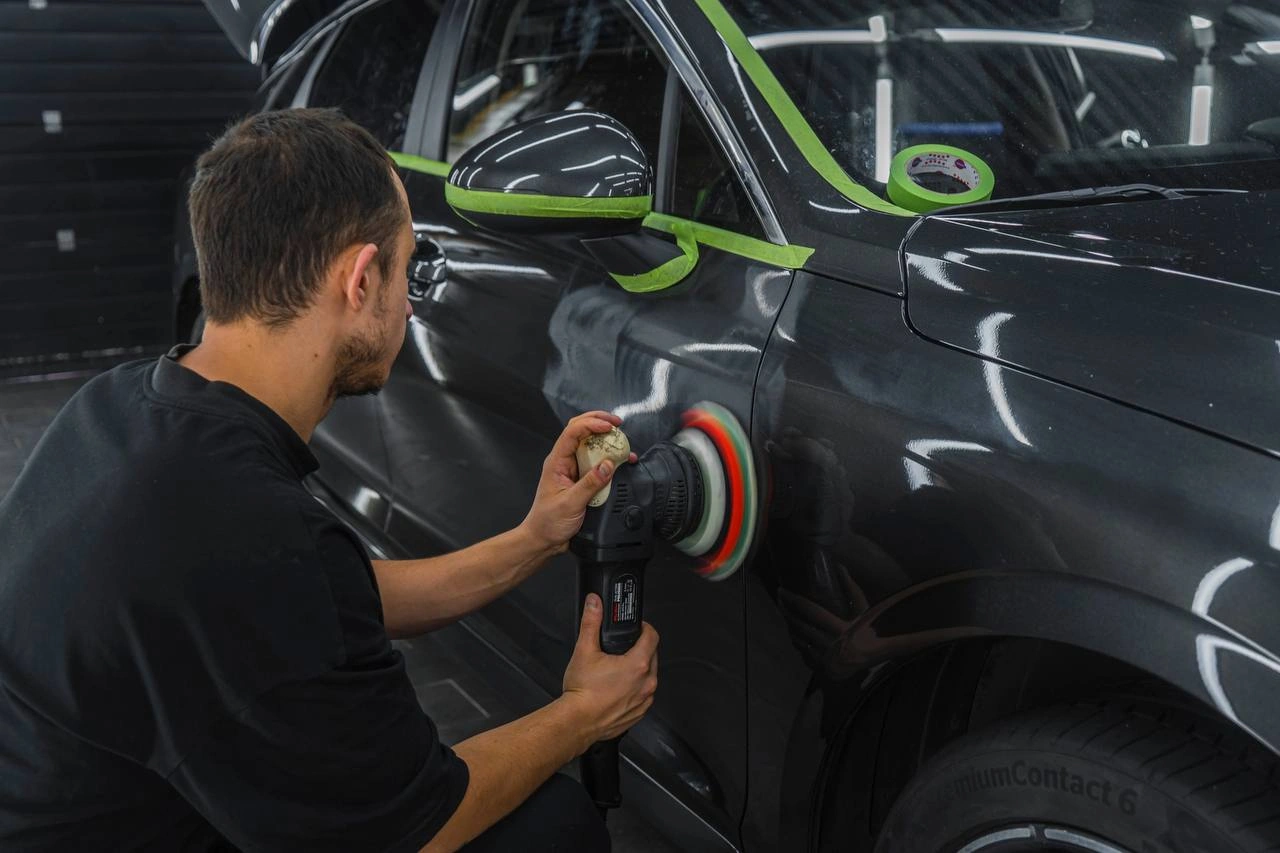 Kia K5 — мастер полирует боковину кузова машинкой рядом с заклеенными кромками отделки