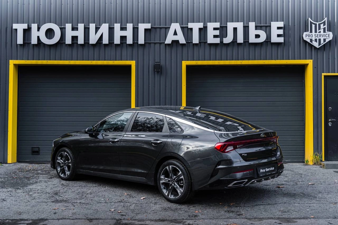 Kia K5 — тёмный седан сзади под углом, боковая линия кузова и задние фонари