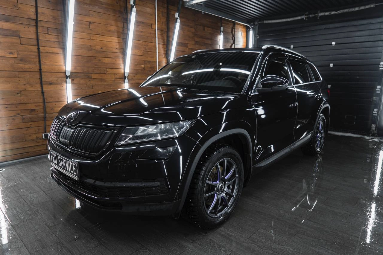 Skoda Kodiaq — чёрный кроссовер спереди под углом в боксе с вертикальным освещением