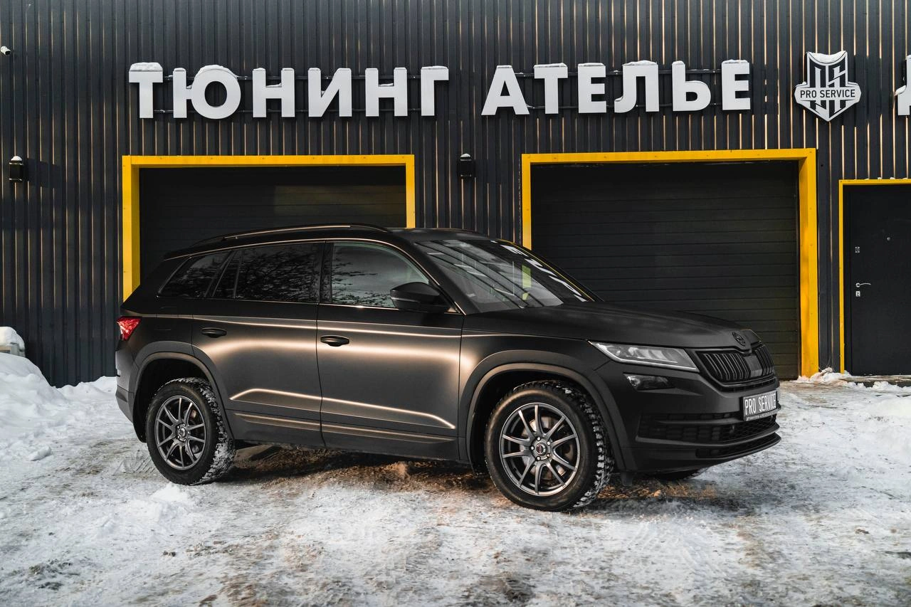 Skoda Kodiaq — тёмный кроссовер сбоку под углом на заснеженной площадке у ателье