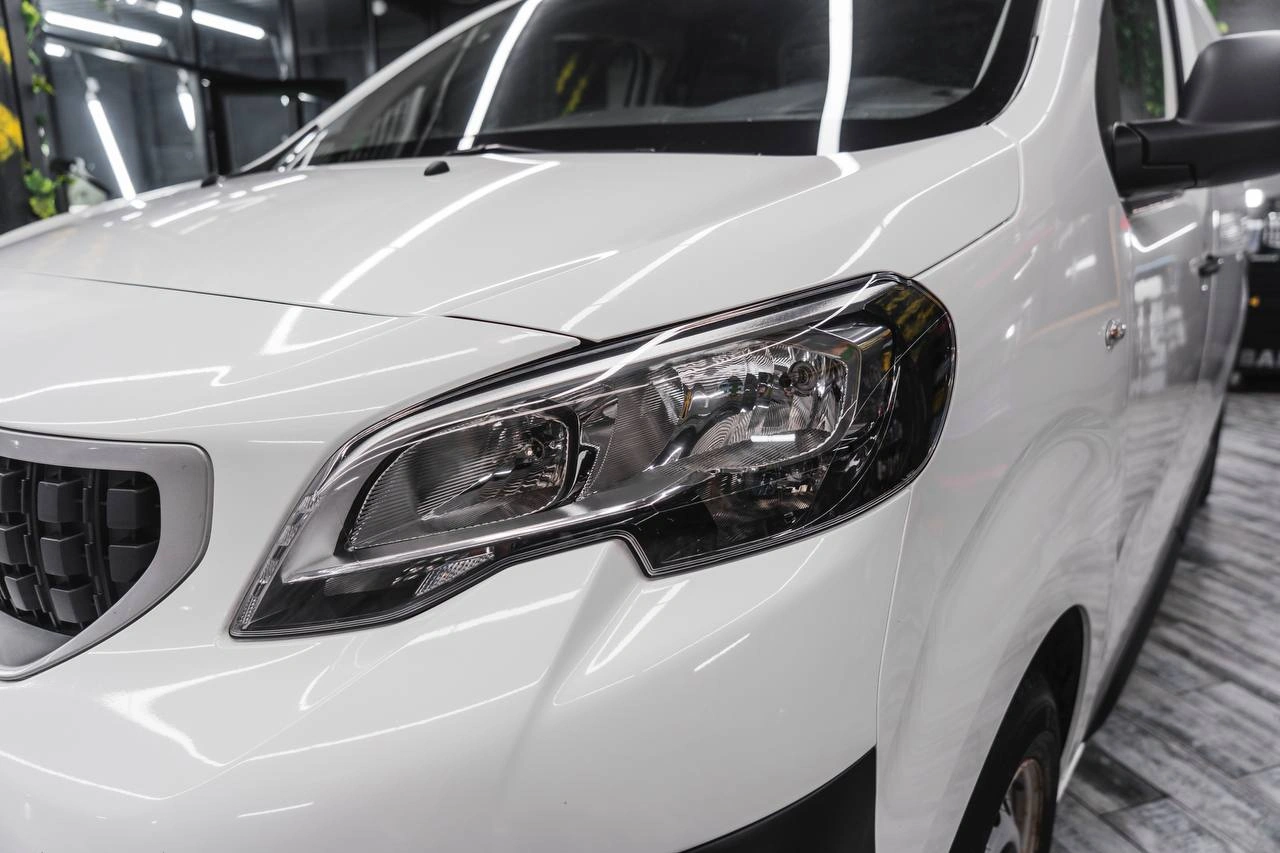 Передняя фара белого Peugeot Expert крупным планом: светлые внутренние секции, кромка капота и переднее крыло.