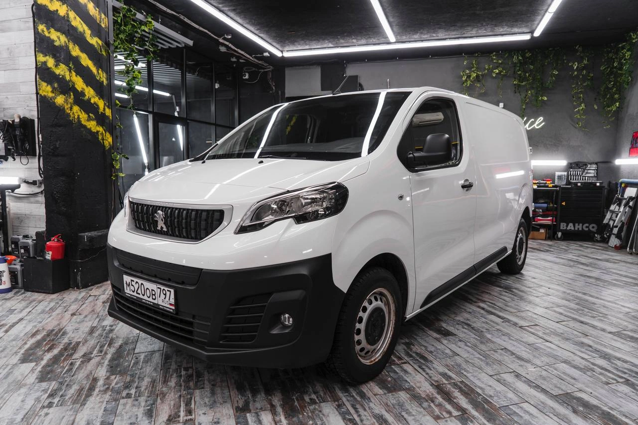 Белый Peugeot Expert в студии: вид спереди и сбоку, чёрный бампер и колёса без декоративных колпаков.