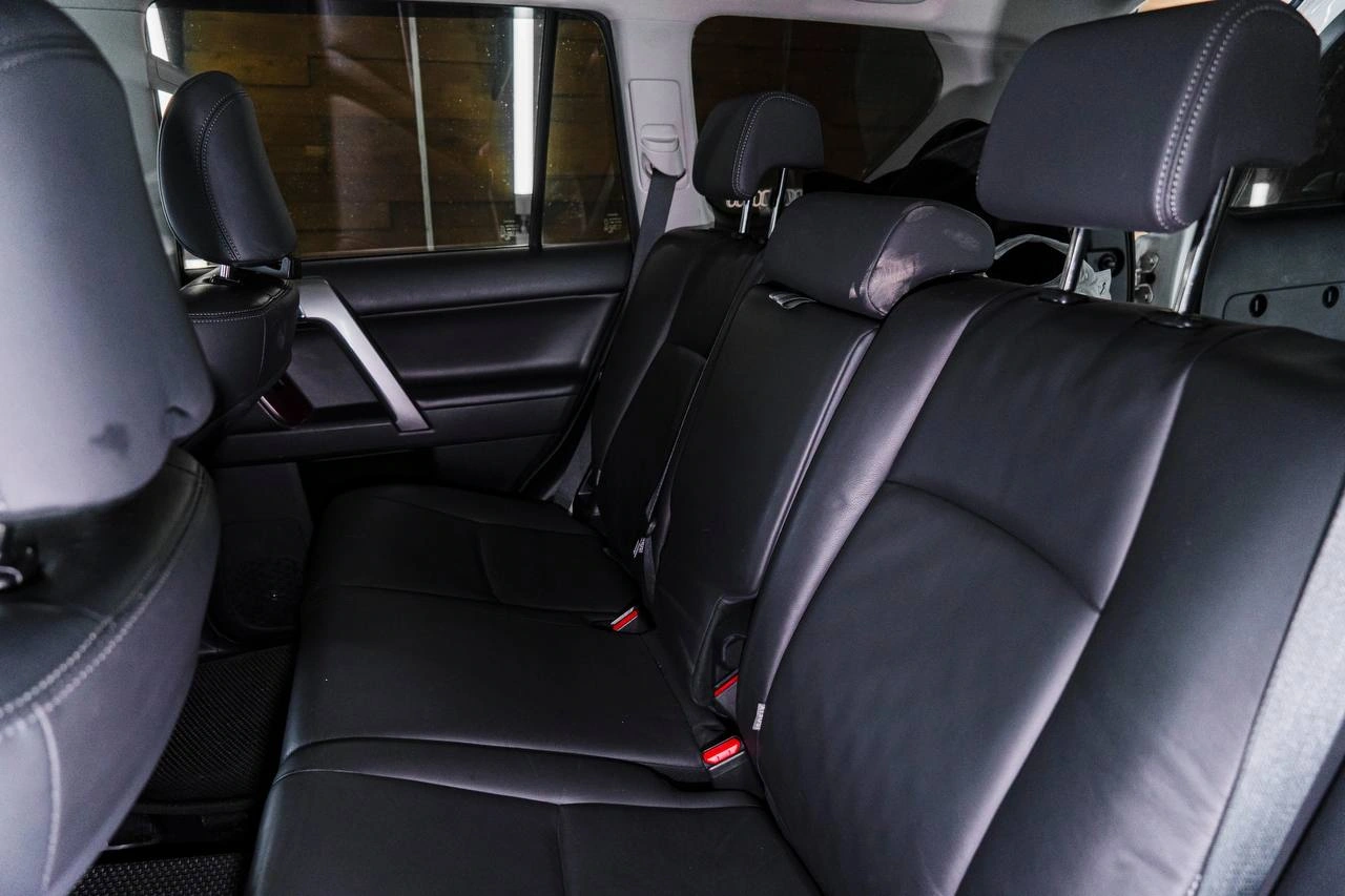 Задний ряд Toyota Land Cruiser Prado с гладкой тёмной обивкой сидений и тремя подголовниками.
