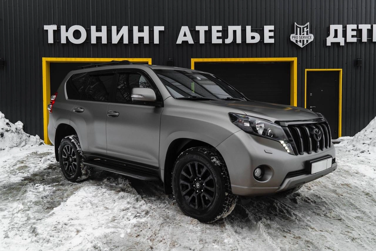 Серый Toyota Land Cruiser Prado с чёрными колёсами, вид спереди под углом на снегу у студии.