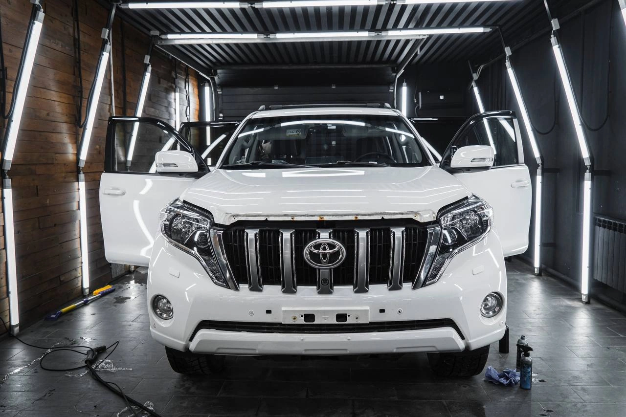 Белый Toyota Land Cruiser Prado с открытыми передними дверями, прямой вид спереди в боксе.