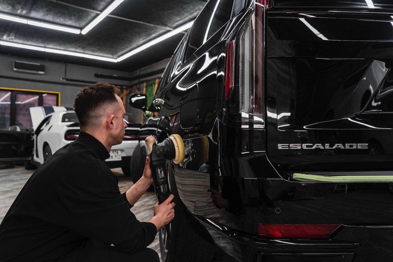 Полировка задней части Cadillac Escalade: мастер обрабатывает чёрную кузовную панель рядом с вертикальным фонарём.