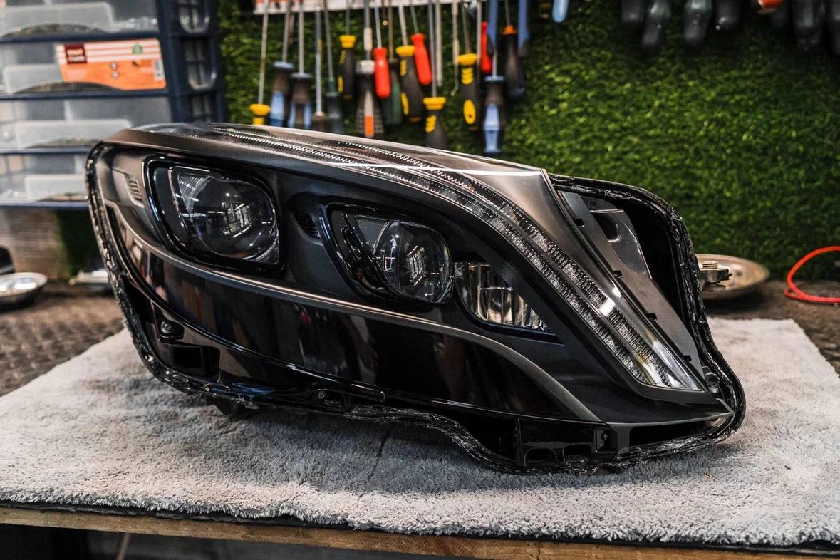 Снятая фара Mercedes-Benz W222 на рабочем столе: крупный план внутренних секций и тёмного корпуса оптики.