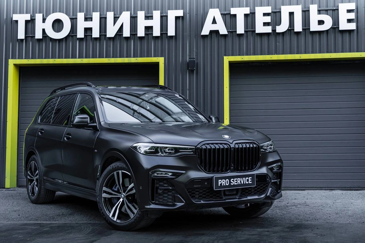 Тёмный BMW X7 с матовой фактурой кузова, вид спереди под углом у входа в студию.