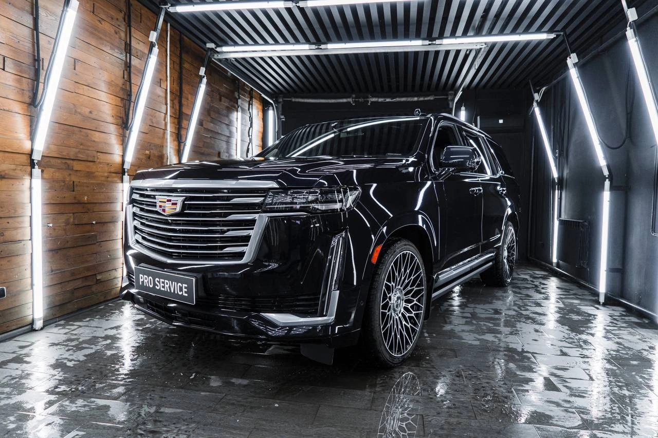 Cadillac Escalade — глянцевый чёрный внедорожник спереди под углом в моечном боксе