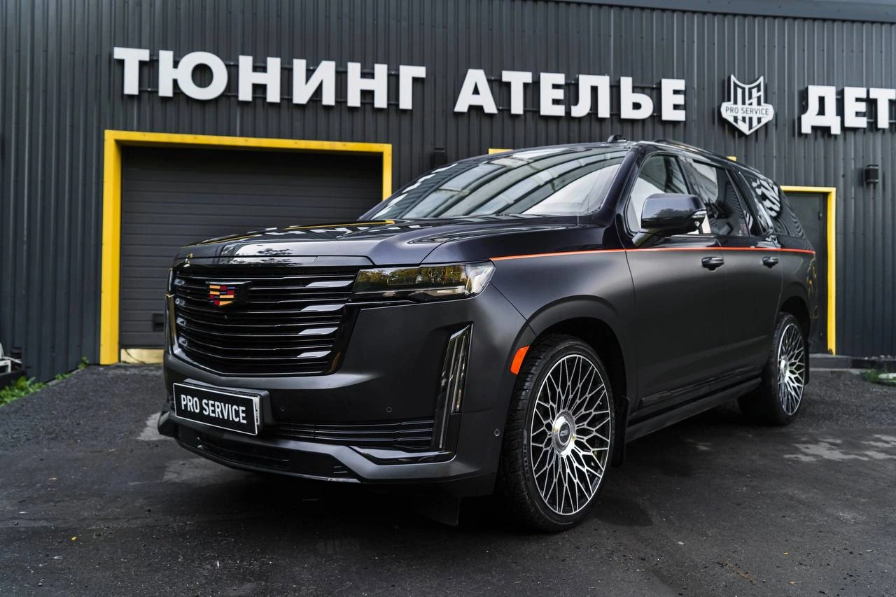 Cadillac Escalade — тёмный внедорожник с чёрной решёткой радиатора спереди под углом у ателье