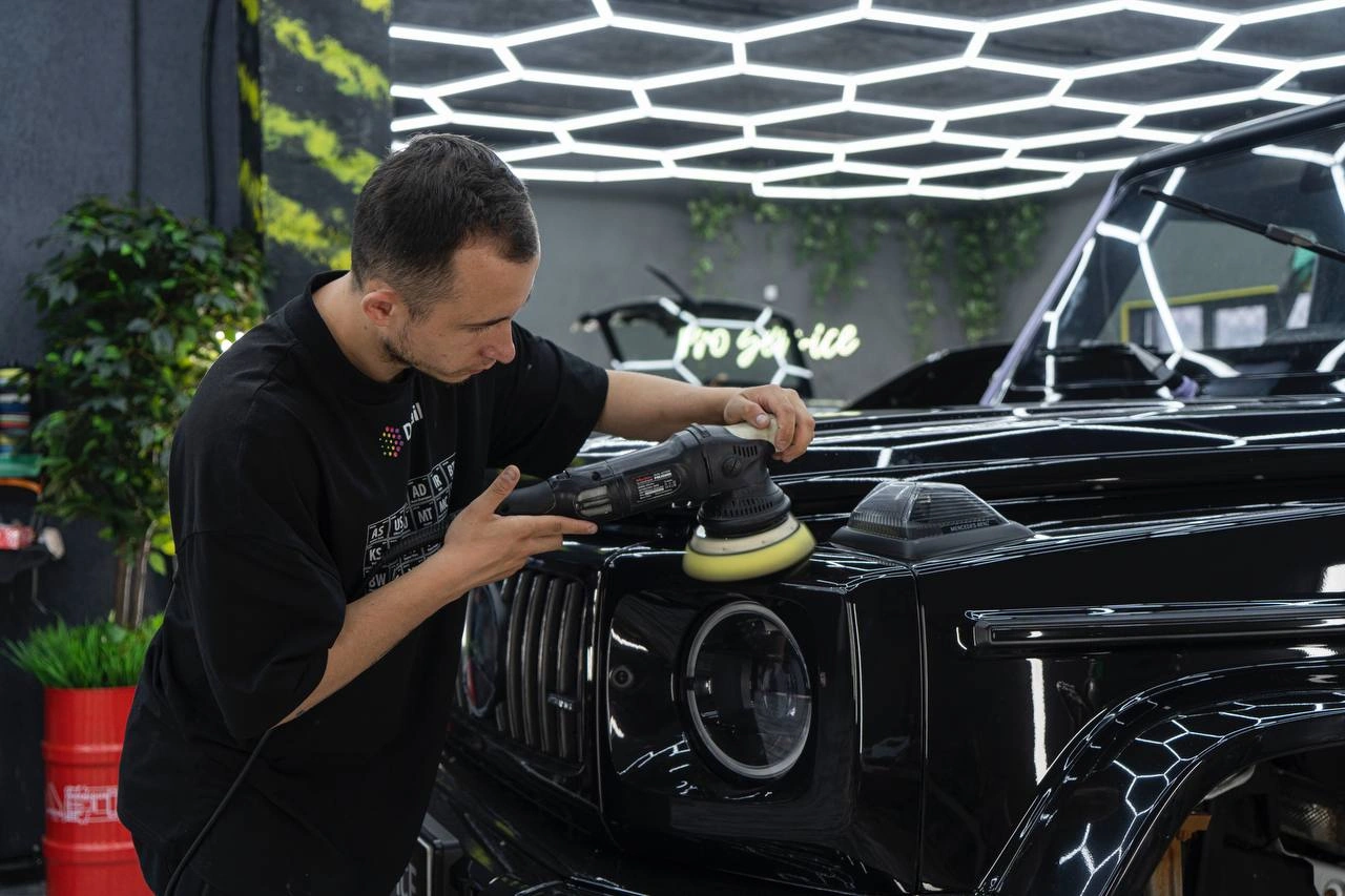 Мастер полирует переднее крыло Mercedes-benz G63 AMG машиной с круглым диском рядом с фарой.