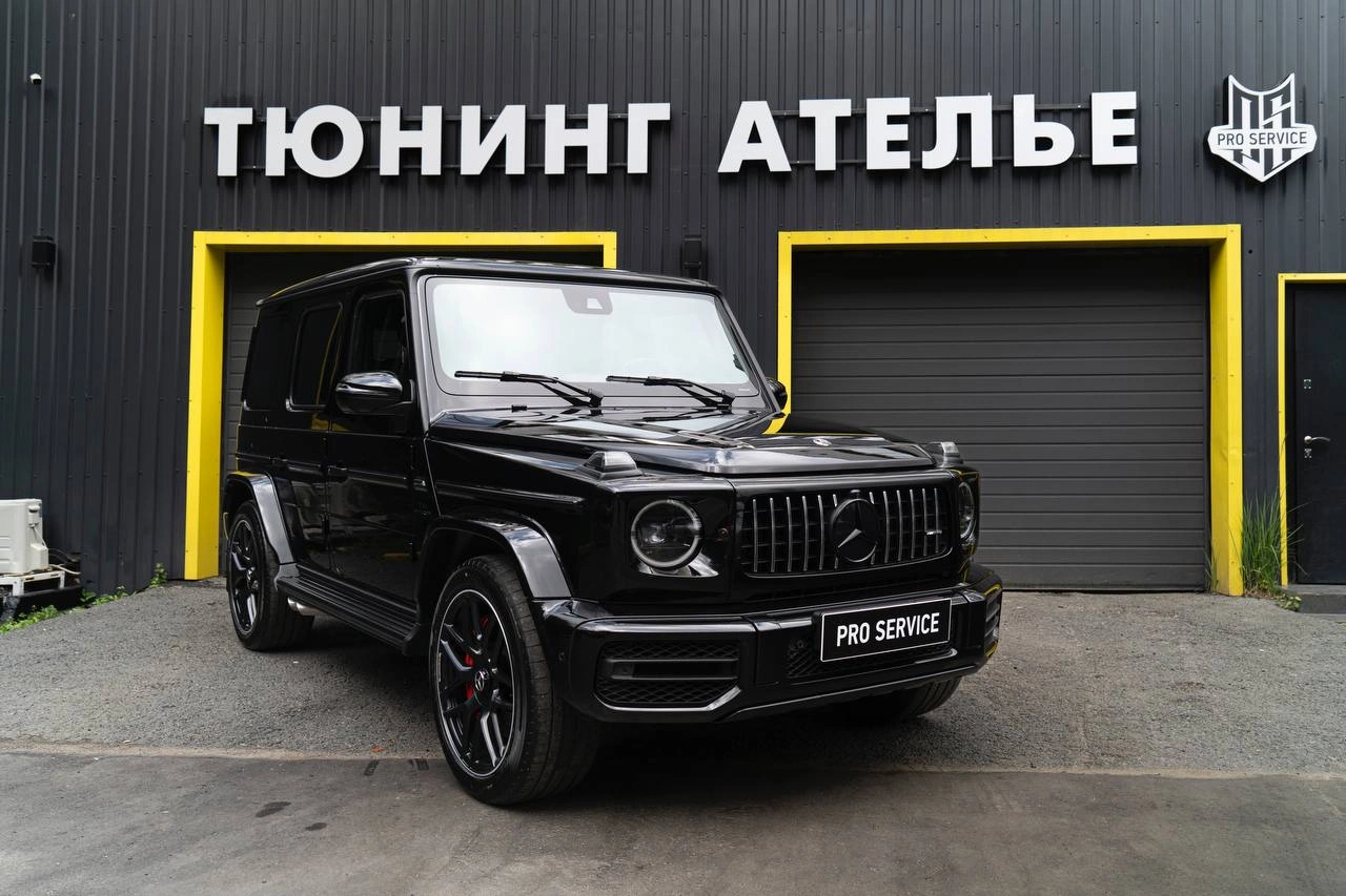 Чёрный Mercedes-benz G63 AMG у входа в ателье: вид спереди и сбоку, вертикальная решётка и широкие колёса.
