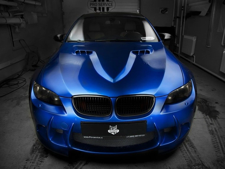 BMW M3 спереди крупным планом: синий капот с воздухозаборниками, тёмная решётка и передний бампер.