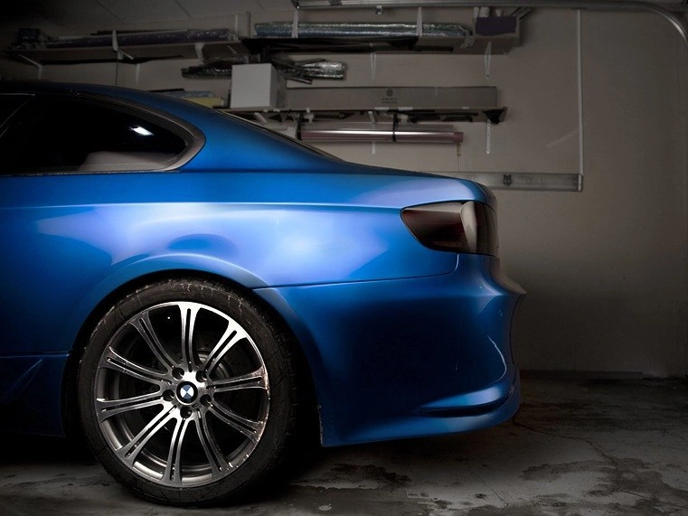 Заднее крыло и колесо синего BMW M3 крупным планом в студии, рядом виден край заднего бампера.