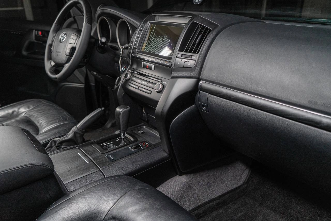 Салон Toyota Land Cruiser 200 с чёрной кожей и декоративными вставками под дерево.