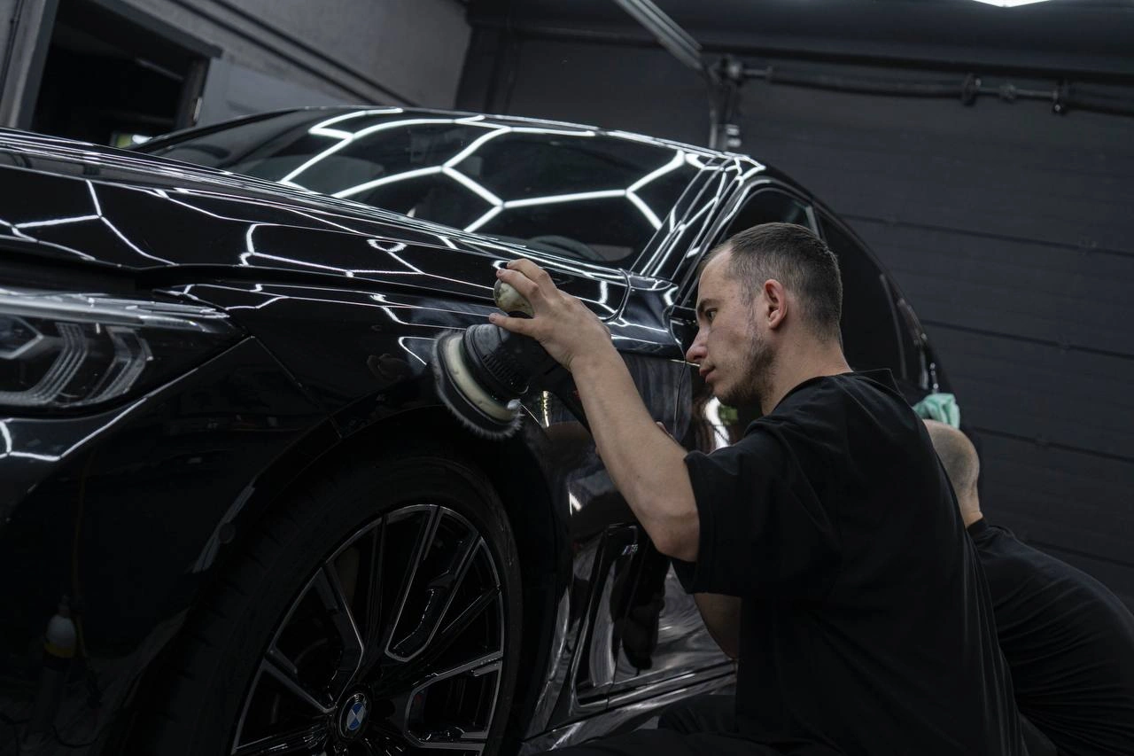 Мастер полирует переднее крыло чёрного BMW 7-й серии над колёсной аркой.