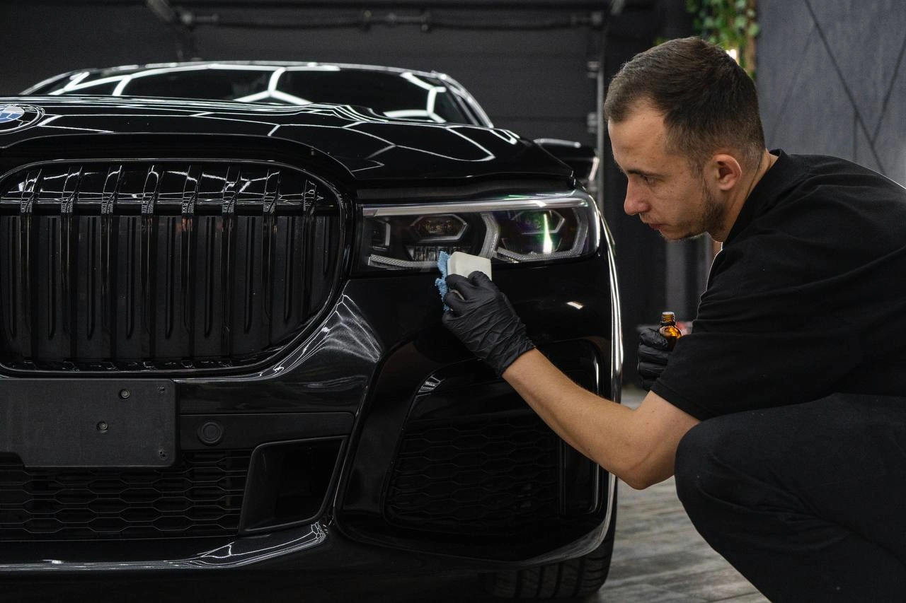 Мастер обрабатывает переднюю фару BMW 7-й серии небольшим аппликатором.