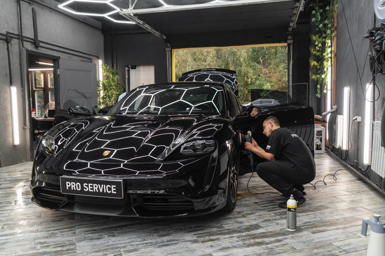 Мастер полирует боковую часть чёрного Porsche Taycan Turbo рядом с передним колесом.