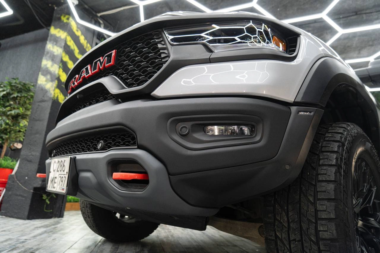 Передний бампер Ram TRX снизу крупным планом: решётка RAM, противотуманные фары и яркая буксировочная петля.