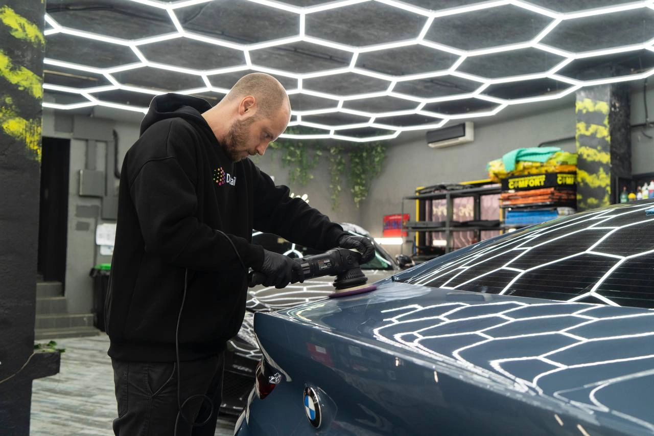 BMW 8-й серии — мастер полирует крышку багажника машинкой под ярким освещением