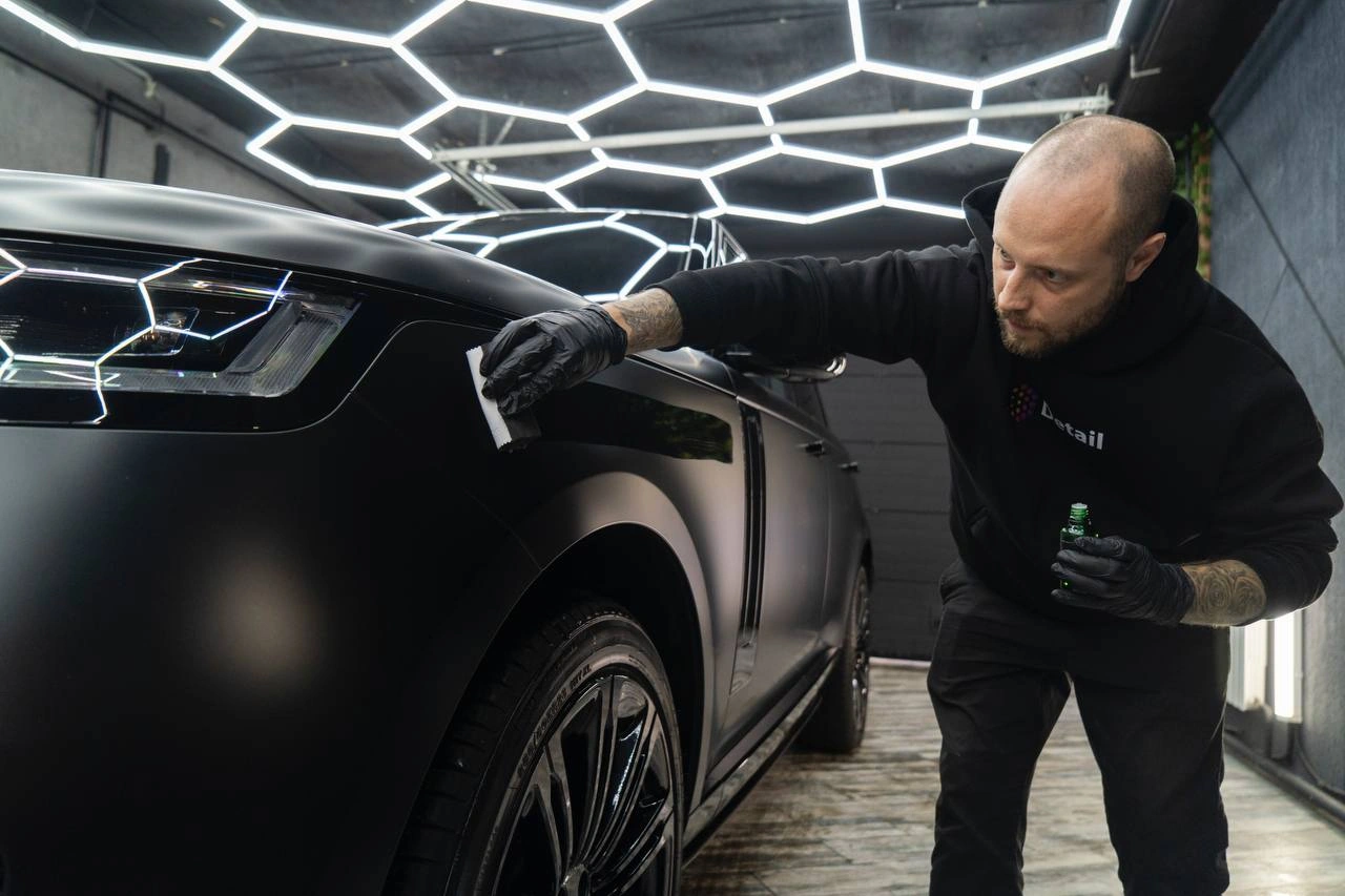 Мастер наносит состав аппликатором на переднее крыло Range Rover рядом с фарой.