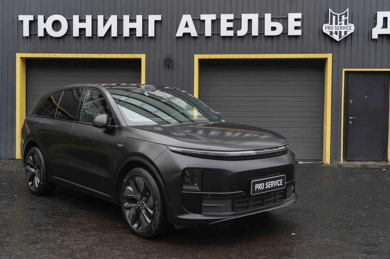 Серый Lixiang L6 у ворот ателье: вид спереди и сбоку, матовая поверхность кузова и тёмные колёса.