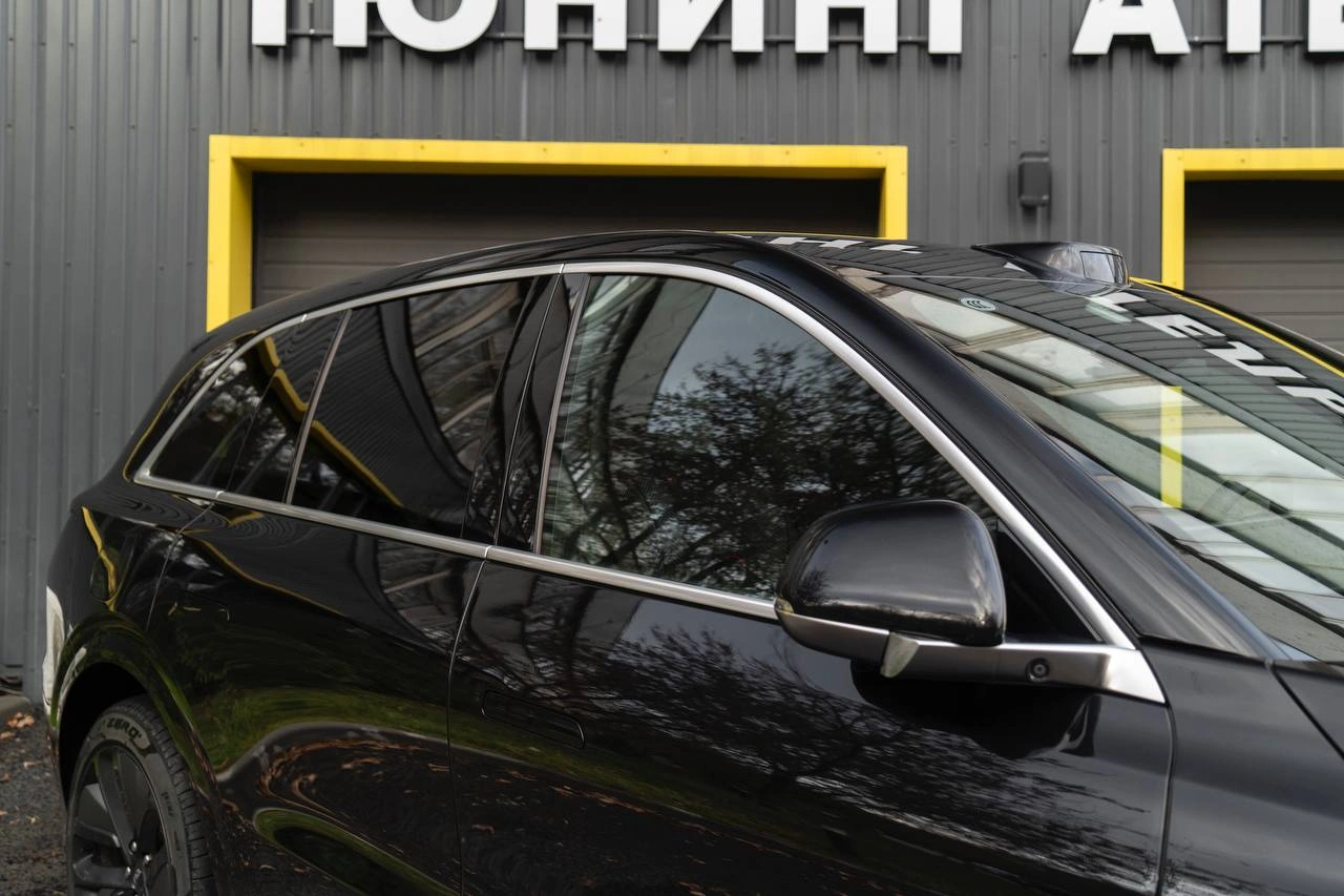 Боковые окна и наружное зеркало чёрного Lixiang L6 крупным планом: в глянцевом кузове отражаются деревья.