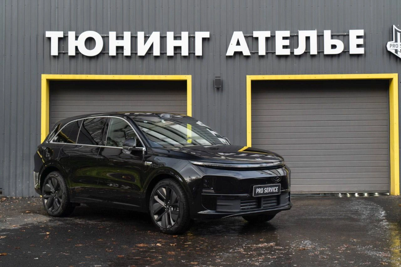 Чёрный Lixiang L6 у входа в ателье: вид спереди и сбоку, на кузове отражается фасад здания.