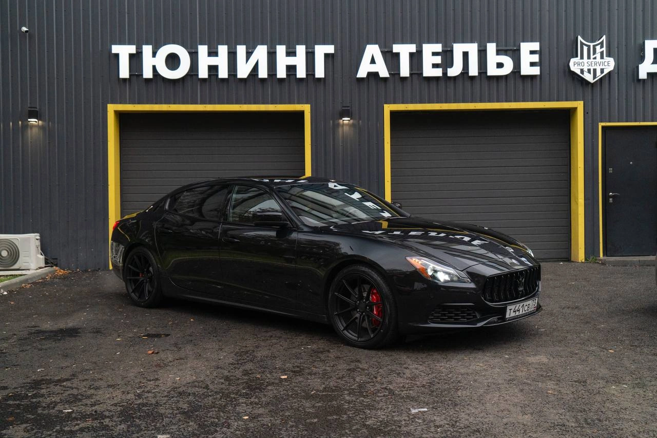 Maserati Quattroporte — чёрный седан спереди под углом на площадке перед тюнинг-ателье