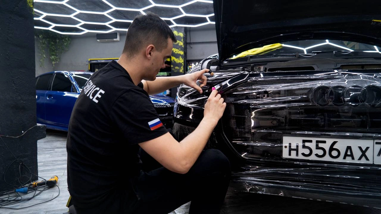 Audi Q8 — мастер разглаживает плёнку на элементах передней части кузова у решётки радиатора