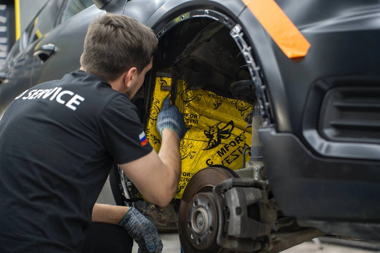 Мастер прикатывает виброизоляцию внутри передней колёсной арки Volvo XC40.