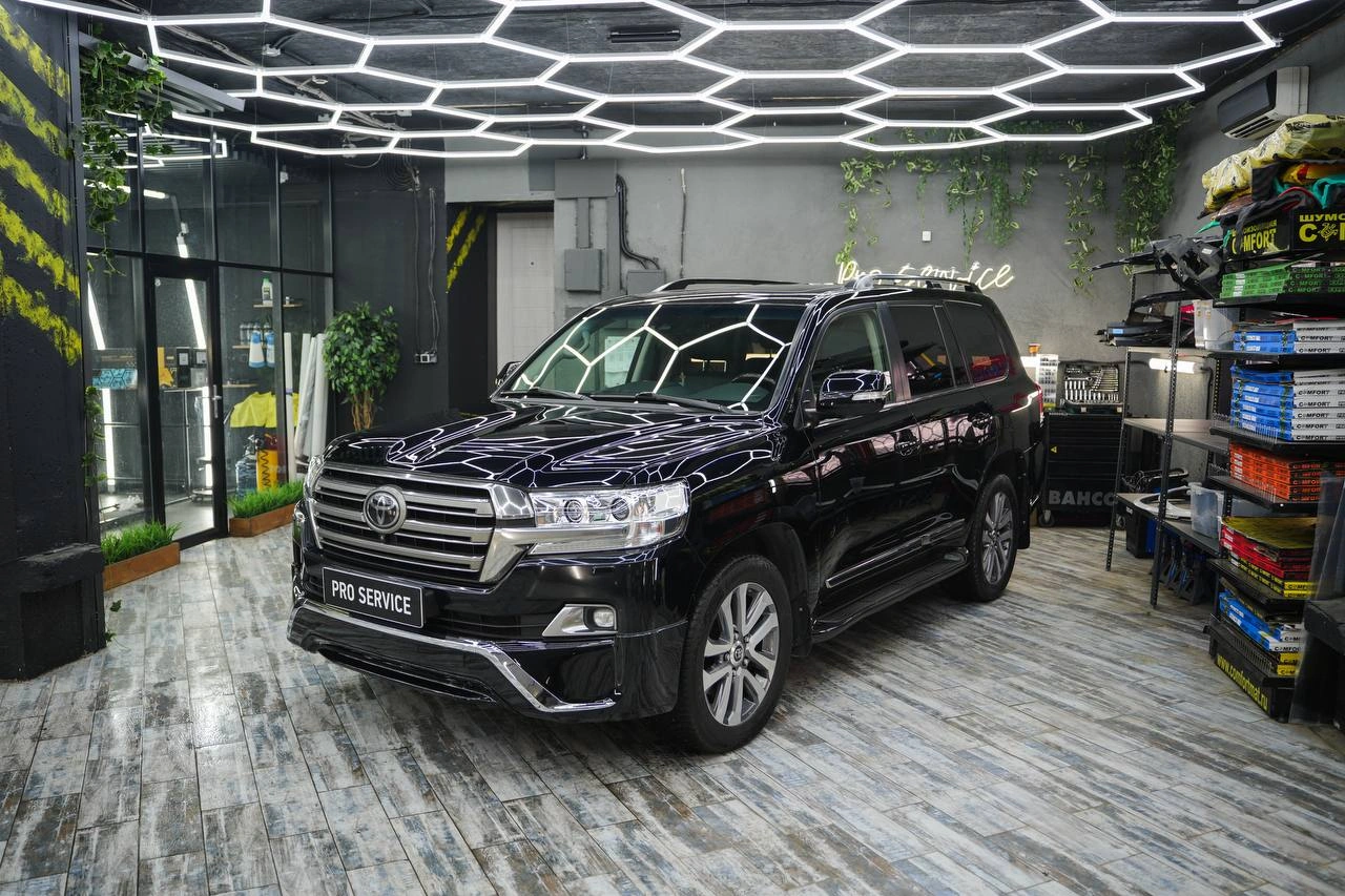 Чёрный Toyota Land Cruiser 200 с отражениями потолочного света, общий вид спереди под углом.