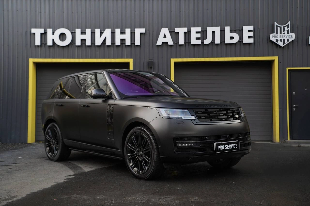 Range Rover с матовой фактурой тёмного кузова, вид спереди под углом у ворот студии.