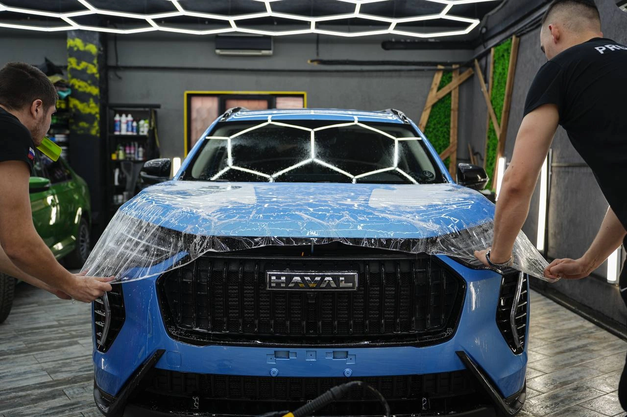 Мастера растягивают прозрачную защитную плёнку на капоте Haval Jolion.