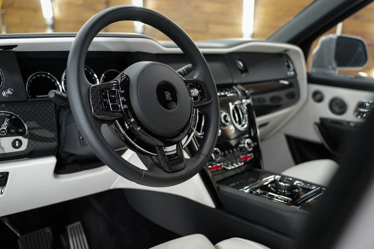 Передняя часть салона Rolls-Royce Cullinan: тёмный руль, светлая панель и глянцевая центральная консоль.