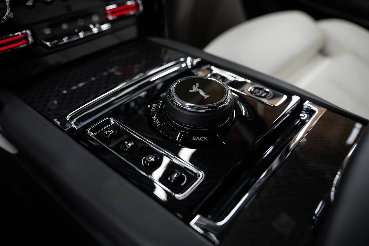 Глянцевая центральная консоль Rolls-Royce Cullinan крупным планом: круглый контроллер и кнопки управления.