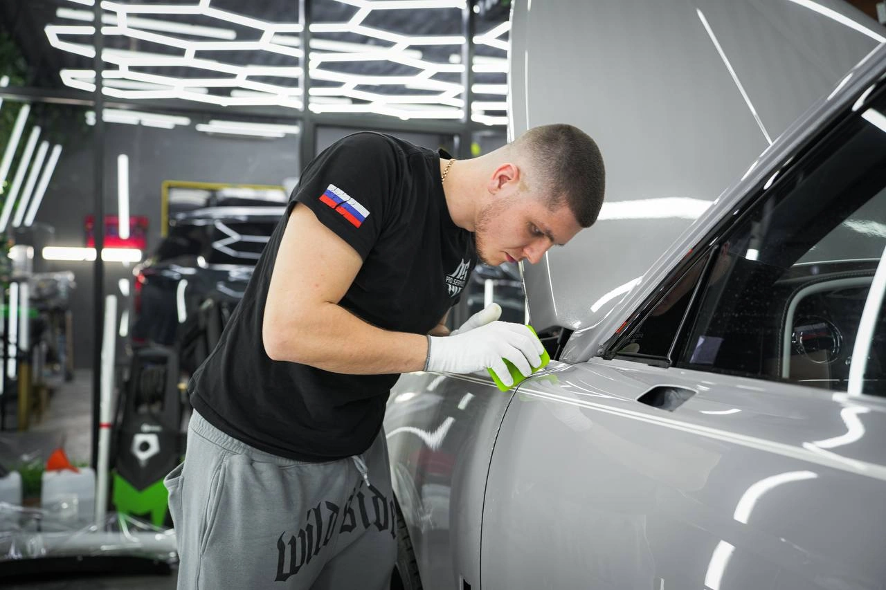 Мастер подгоняет плёнку на верхней кромке передней двери Rolls-Royce Cullinan рядом с боковым стеклом.