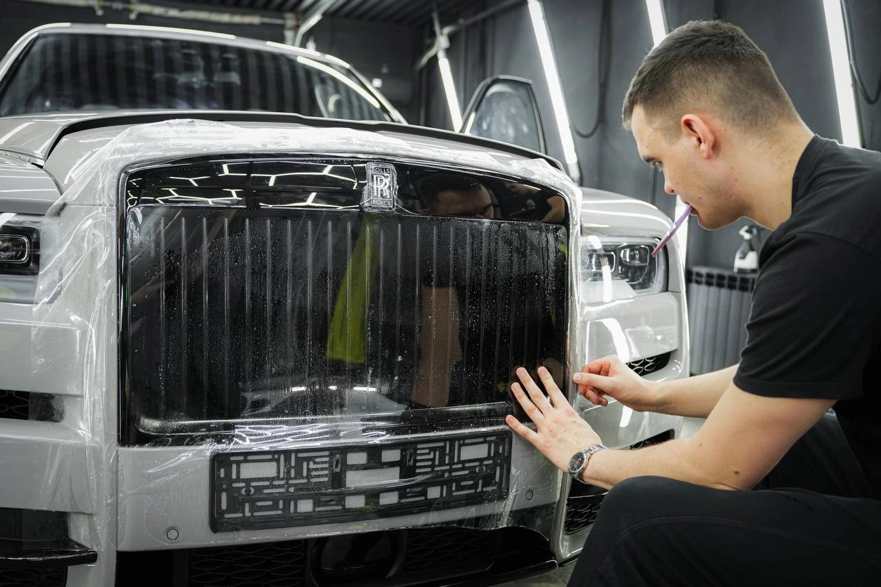 Оклейка решётки радиатора Rolls-Royce Cullinan: мастер подгоняет прозрачную плёнку на передней части автомобиля.