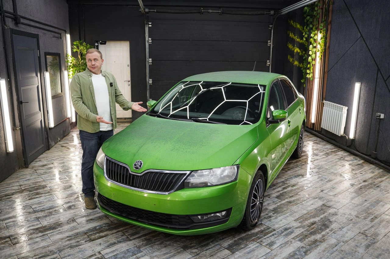 Skoda Rapid — зелёный седан спереди под углом, рядом стоит человек в рабочем боксе