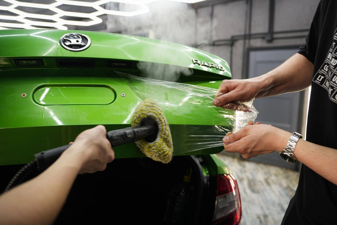 Skoda Rapid — мастера снимают старую плёнку с открытой крышки багажника