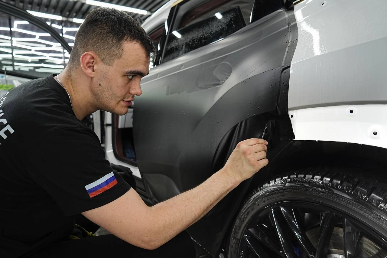 Мастер подгоняет плёнку по краю переднего крыла и колёсной арки BMW XM.