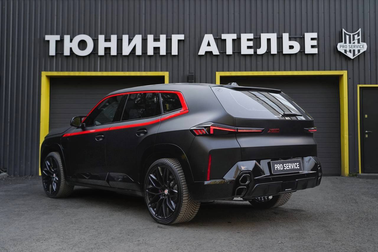 Задняя часть BMW XM после оклейки: тёмный кузов и красные акценты отделки.