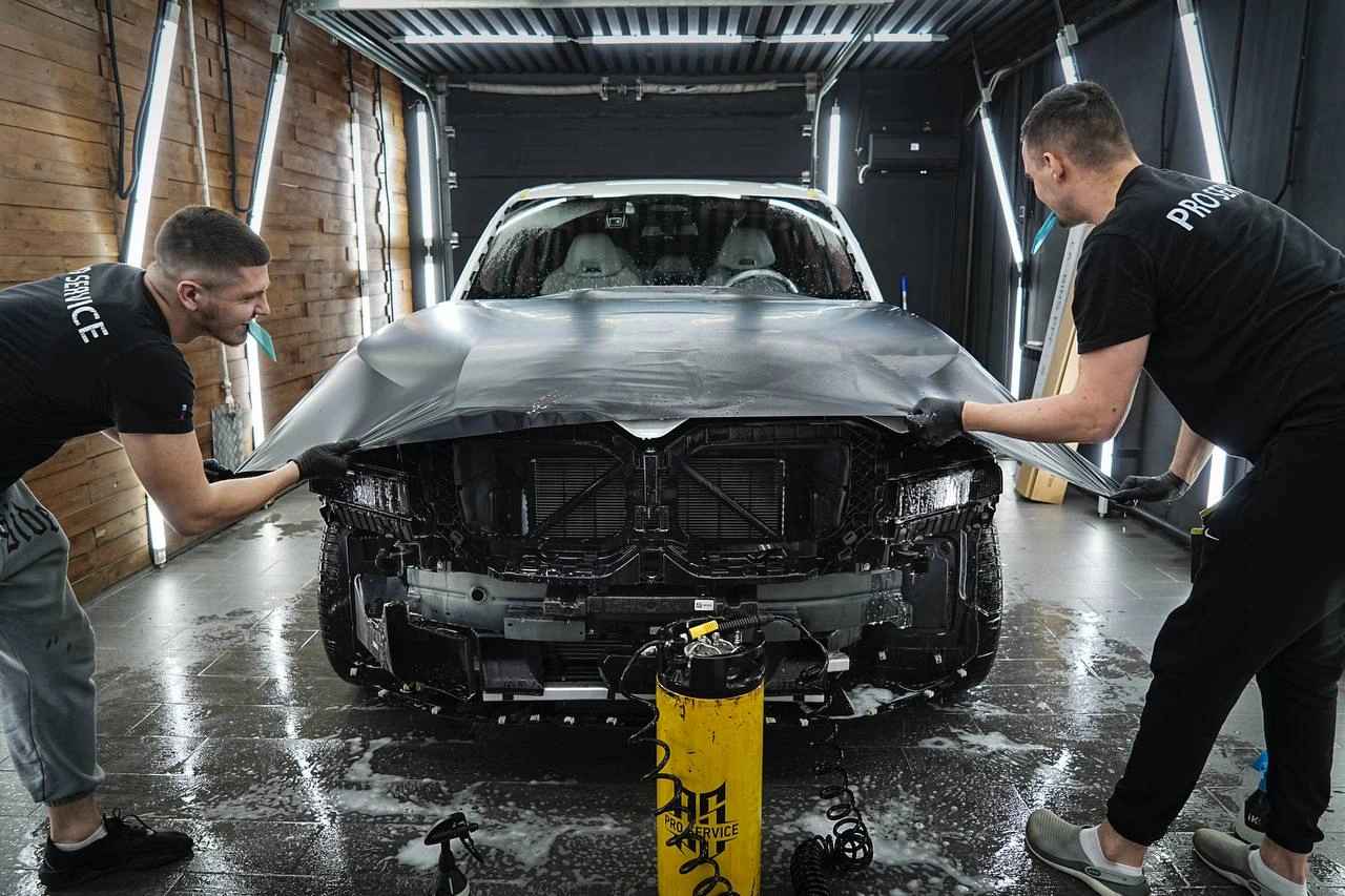 Мастера укладывают тёмную плёнку на капот BMW XM со снятым передним бампером.