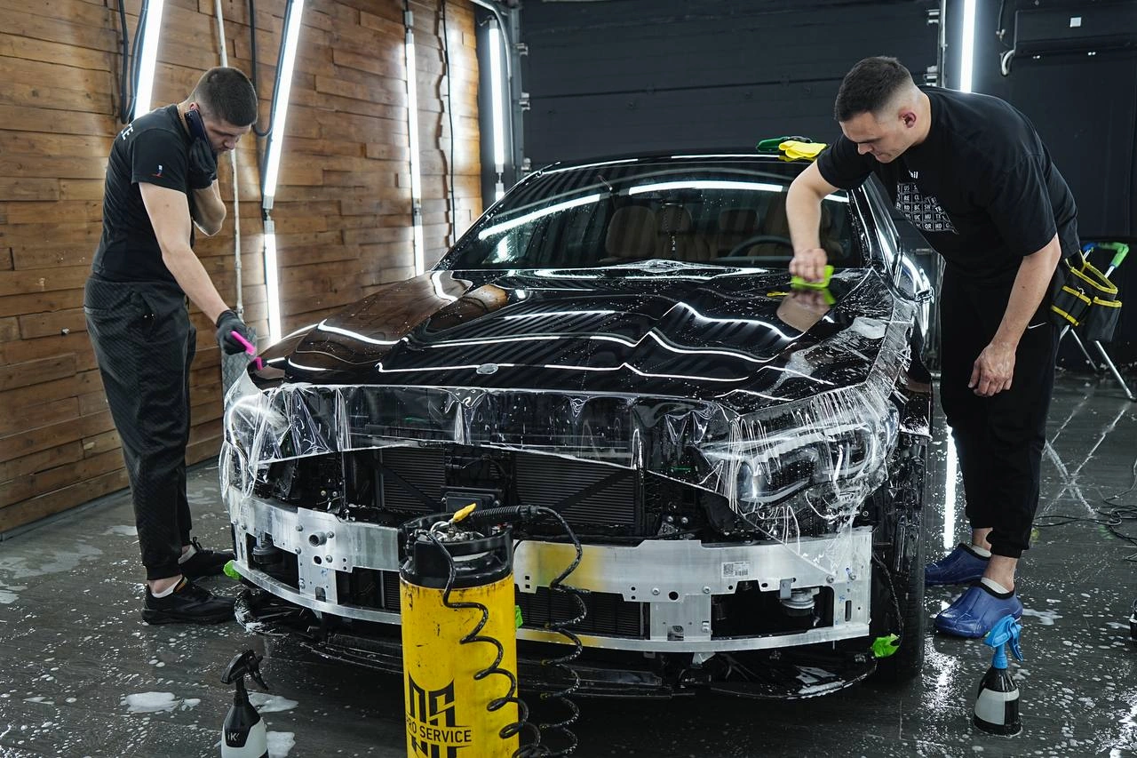 Мастера оклеивают переднюю часть Mercedes-Benz E класса со снятым бампером и открытым усилителем.