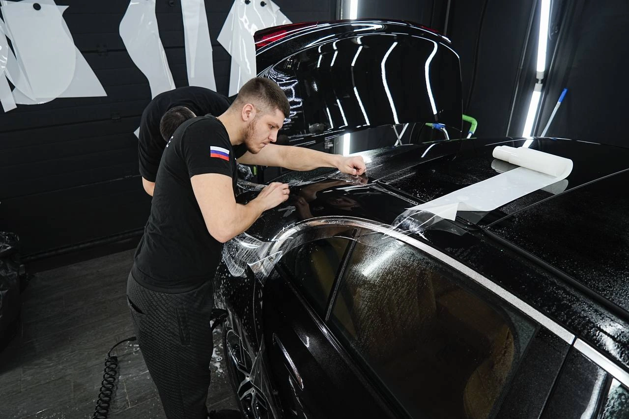 Оклейка Mercedes-Benz E класса: мастер подгоняет прозрачную плёнку на кузовной панели.