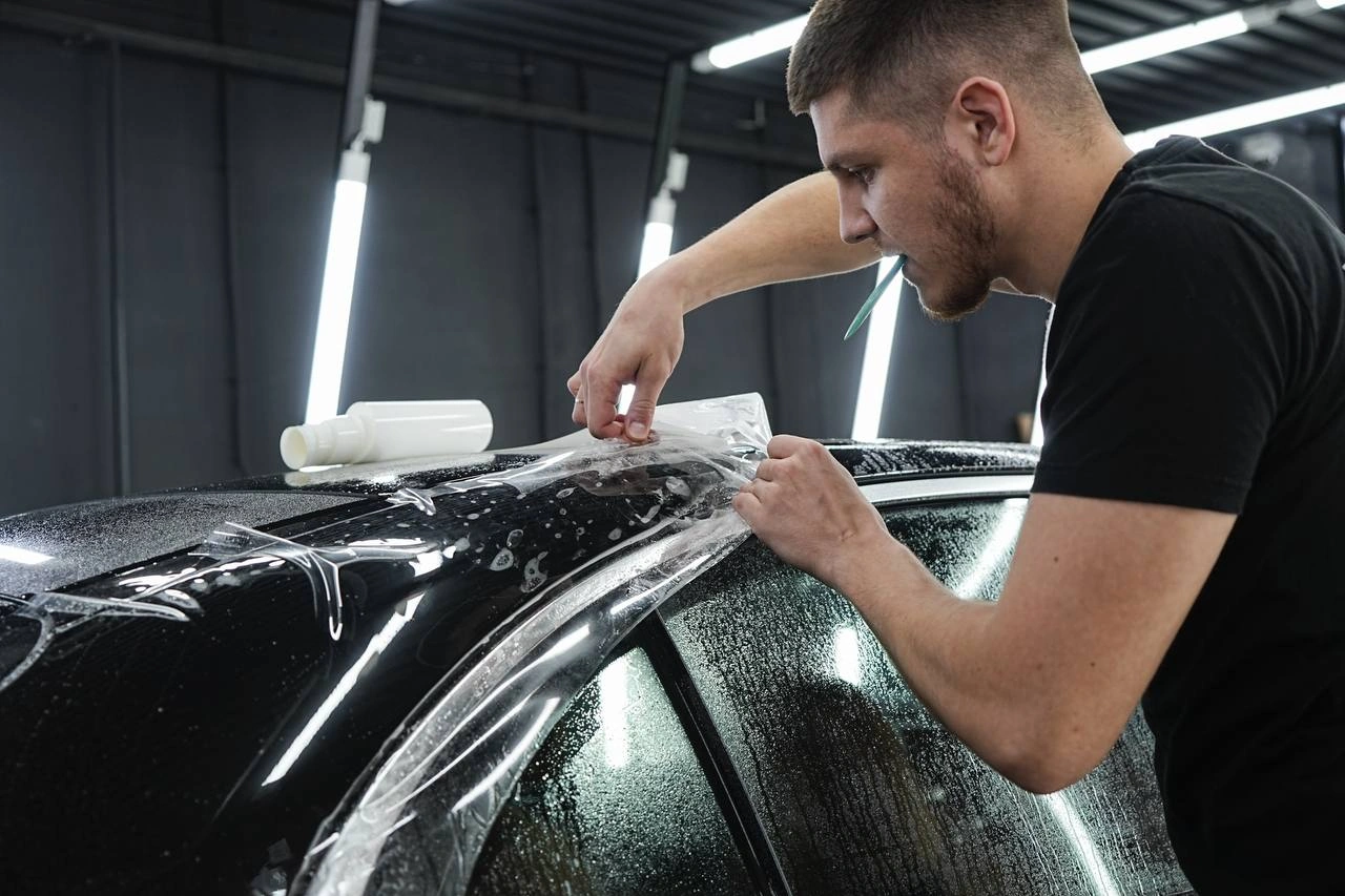 Мастер натягивает прозрачную плёнку на верхнюю часть кузова Mercedes-Benz E класса.