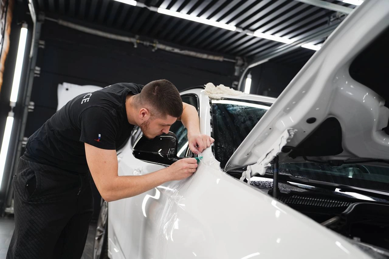 Мастер работает у переднего крыла белого BMW X3 под открытым капотом, крупный план кромки кузовной панели.