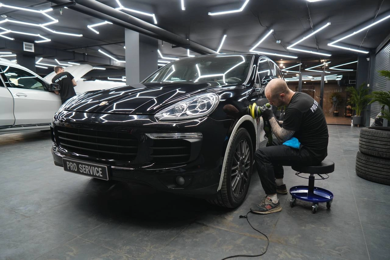 Мастер полирует переднее крыло чёрного Porsche Cayenne рядом с колёсной аркой.