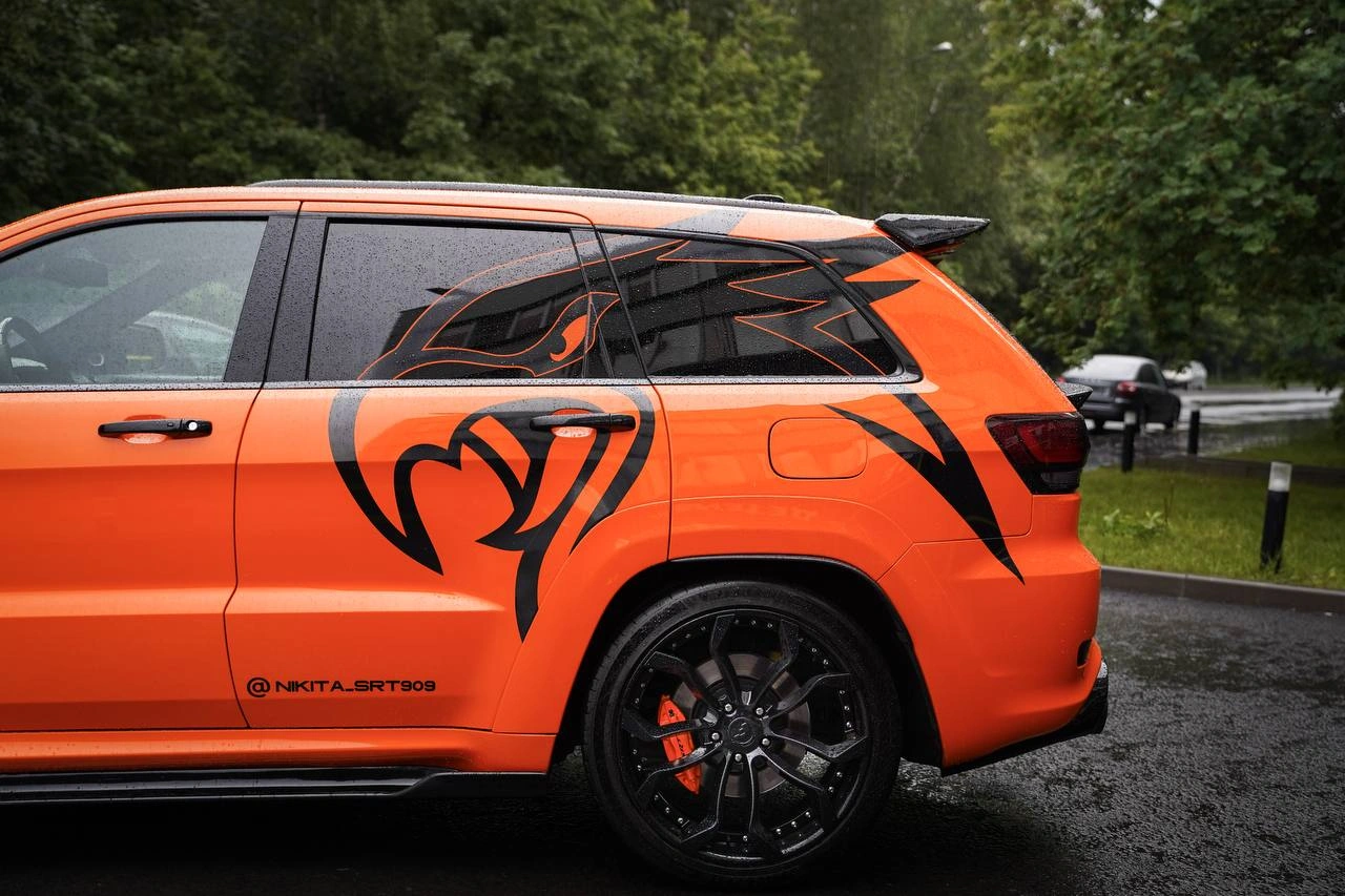 Боковая часть Jeep Grand Cherokee SRT: крупная чёрная графика на оранжевом кузове и тёмное заднее колесо.